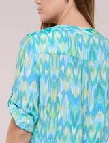 Blusa camisera de estilo casual confeccionada en mezcla de rayón y poliéster, con estampado multicolor en tonos turquesa, verde y celeste. Presenta escote en V con cuello mao, abotonadura frontal con botones nacarados, bolsillos aplicados en el pecho y mangas tres cuartos con presilla para arremangar. Cuenta con ruedo curvo y picos frontales diseñados para anudar en la cintura.