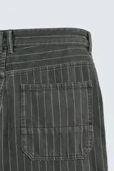 Pantalón de corte ancho (baggy fit) color verde oscuro/gris oscuro con finas rayas verticales blancas. Presenta cintura ajustable con trabillas laterales, bolsillos delanteros, bolsillos traseros de plastrón, bolsillo cerillero y una tira multifunción en la pernera.
