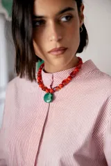 Collar corto compuesto por cuentas de cristal checo en tonos rojos de diversas formas y tamaños, con un medallón central circular de cristal checo en color verde. Incluye cadena de ajuste para regular el largo.