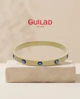 Esclava rígida de acero con baño de oro, decorada con cinco dijes de ojo turco incrustados. Se presenta junto a una pulsera de cadena fina con un dije de mano de Fátima.