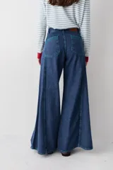 Jean de corte wide leg con tiro alto, confeccionado en denim azul oscuro. Presenta costuras verticales a lo largo de las piernas con pespuntes en color verde a contratono.
