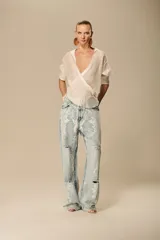 Pantalón de jean de tiro medio y corte recto, con lavado claro y aplicación de encaje floral blanco que cubre toda la prenda. Presenta roturas en las rodillas y muslos.