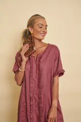 Vestido tipo túnica largo de lino, color bordo, con mangas cortas, bolsillos laterales y detalle de volados en la botonera frontal.