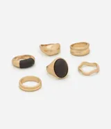 Kit de seis anillos de diseño variado con acabado en tono oro batido. Incluye piezas con estructuras irregulares, formas redondeadas y detalles en poliuretano (PU) en tono oscuro, elaborados en metal reciclado.
