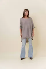 Maxi sweater tejido color beige con efecto metalizado sutil, silueta amplia, mangas tipo murciélago y largo asimétrico (más corto adelante y más largo atrás).