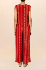 Chaleco rojo con estampado de cadenas doradas, sin mangas y con cuello redondo. Cierre frontal con ojales, botones dorados y cordones entrelazados.