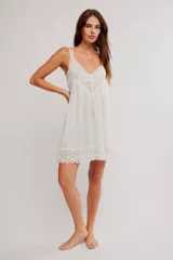 Vestido corto tipo slip dress color blanco, de corte amplio tipo babydoll, confeccionado en mezcla de viscosa y algodón. Presenta escote en V con apliques de encaje, tiras finas regulables y ruedo festoneado con detalles de encaje y calados.