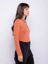 Top color beige de manga larga con cuello camisero y abertura ovalada en el escote. Su tela es flexible y consta de finas fibras metálicas.