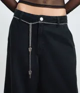 Bermuda tipo jorts de tiro bajo, confeccionada en denim de algodón. Presenta un corte recto y estructurado, con bolsillos funcionales, trabillas en la cintura y un cinturón decorativo de cadena metálica.