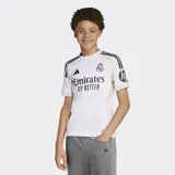 Camiseta de fútbol Adidas del Real Madrid, primera equipación temporada 25/26. Diseño en color blanco con detalles en negro y líneas amarillas sutiles, cuello redondo y mangas cortas. Incluye el escudo del club bordado y el logo de la marca.