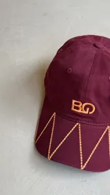 Gorra de gabardina color bordó con bordados color naranja en el frente y en la visera.