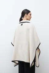 Capa de paño color crema con bordes en contraste negro. Presenta cierre frontal con alamares de cuero sintético y bolsillos laterales amplios.