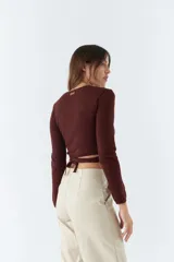 Top tejido de punto con diseño cruzado, escote en V y mangas largas. Cuenta con tiras para anudar en la cintura y detalle de grifa de cuero.