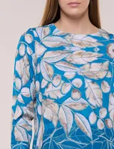 Blusa de silueta holgada y corte recto con caída fluida, escote redondo y mangas largas con puños anchos estructurados, con estampado floral en tonos pasteles sobre fondo blanco.