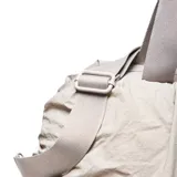 Bolso deportivo de gran capacidad con diseño arrugado, color gris claro. Cuenta con doble asa superior, correa ajustable y desmontable, y correas en la base para sujetar accesorios. Incluye compartimento principal con cierre, bolsillo frontal y bolsa interior desmontable.
