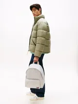Mochila de diseño redondeado en color gris claro, confeccionada en poliéster texturizado. Cuenta con un compartimento principal con cierre, un bolsillo exterior con cremallera en la parte frontal y un bolsillo interior de malla abierto. Posee asa superior y correas ajustables y acolchadas. Lleva un parche tejido de Tommy Jeans en la parte delantera.