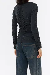 Camiseta negra de corte ajustado con escote pico y manga larga ajustada y fruncida. Presenta túneles fruncidos en delantero y espalda, y strass por toda la prenda.