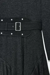 Vestido midi de cuello redondo y manga larga, confeccionado en tejido de punto gris oscuro. Presenta un cinturón integrado con hebilla y aplicación de tachas metálicas, y un bajo con diseño asimétrico y volados.