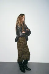 Pantalón bombacho de tiro medio con estampado a cuadros en tonos verde militar, negro y blanco. Presenta bolsillos laterales ocultos, cierre frontal con cremallera y botón, y bajo abullonado con puño y botón.