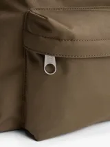 Mochila de diseño redondeado en color marrón, confeccionada en poliéster texturizado. Cuenta con un compartimento principal con cierre, un bolsillo exterior con cremallera y un bolsillo interior de malla. Incluye asa superior y correas ajustables y acolchadas. Presenta un parche tejido con el logo de Tommy Jeans en la parte delantera.