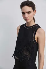 Blusa sin mangas de corte crop en color blanco, con detalles de bordados calados en tono tostado formando diseños florales en el cuello, los hombros y el borde inferior.