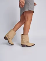 Bota de cuero color marrón con caña media, taco cuadrado y punta fina. Presenta tachas plateadas en el borde superior y en la tira que rodea el tobillo. El cuero tiene un acabado liso y brillante.