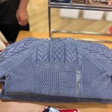 Sweater de punto trenzado color azul, con cuello redondo y diseño de paneles con diferentes texturas. Presenta el nombre de la marca bordado en el centro del pecho.