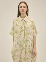 Vestido camisero de corte oversize, con cuello clásico, cierre frontal de botones y mangas cortas. Presenta un estampado floral en tonos verde y beige, bolsillos laterales y un diseño holgado.