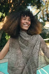 Blusa de cuello subido y manga sisa, confeccionada en tejido fluido semitransparente con estampado de lunares en tonos beige y negro. Presenta un diseño superpuesto tipo capa con caída asimétrica y cierre posterior con abertura y botón.