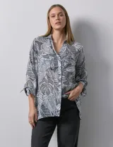 Camisa estampada con hojas en tonos celeste, naranja y verde. Tiene cuello con solapa, abertura central con botones, bolsillos aplicados en la parte delantera y mangas 3/4 con lazo.