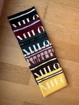 Clutch de neopreno color marrón oscuro con cierre de cremallera metálica dorada. Presenta la inscripción "MILO" en letras blancas de gran tamaño en el frente.