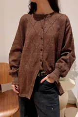 Camisa de punto con acabado brillante, color negro con destellos plateados, diseño de rombos, cuello redondo, cierre frontal con botones y mangas largas con puños ajustados.