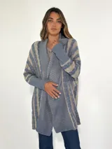 Saco largo de tejido de punto con diseño a rayas horizontales en tonos celeste y beige. Tiene cuello chal y mangas largas.