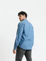 Camisa de denim de algodón con cuello clásico, cierre frontal con botones, bolsillo superior de parche y mangas largas con puños abotonados.