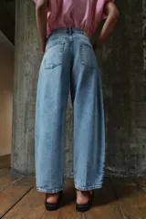 Pantalón de jean tiro medio con diseño barrel, caracterizado por su pernera holgada que se estrecha hacia el tobillo. Presenta cinco bolsillos, cierre frontal con cremallera y botón, y detalle de raya planchada en el frente.