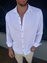 Camisa de manga larga confeccionada en lino, color blanco, con cuello clásico y cierre frontal de botones en tono madera.
