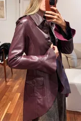 Tapado de cuero ovino color vino, con diseño de corte entallado, mangas largas con volados en los puños y ruedo con volados. Presenta cierre frontal con botones y bolsillos laterales con solapa.