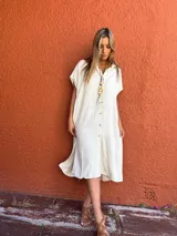 Vestido camisero color crudo, de corte recto y largo midi. Tiene cuello camisero, mangas cortas y cierre frontal con botones.