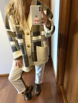 Saco tejido de punto grueso con diseño a cuadros en tonos crema, gris y ocre. Tiene corte oversize, cuello en V, cierre con botones y bolsillos frontales.