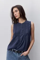 Blusa sin mangas color azul marino, de silueta fluida, con cuello redondo y detalle de alforzas y botones en la parte frontal.