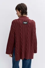 Sweater de punto con diseño de trenzas, cuello alto y mangas largas con puños acampanados. Presenta un corte holgado con terminación asimétrica en el ruedo.