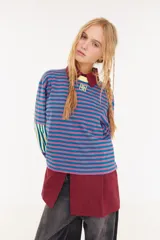 Remera de manga larga con corte boxy, confeccionada en algodón. Presenta un diseño de rayas horizontales en tonos azul y fucsia, con detalles de rayas verticales en los codos, tajos laterales y logo bordado en el pecho.