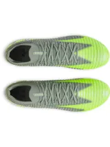 Championes de fútbol Under Armour Shadow Elite 3 FG, diseñados para terreno firme. Presentan una parte superior de tejido IntelliKnit en color gris con detalles en verde neón, logotipo de la marca en negro y suela de fibra de carbono con tapones transparentes.