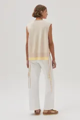 Chaleco tejido de algodón color beige, con escote en V, lazos laterales y terminaciones con pompones.