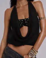 Top halter negro con escote profundo y detalle de frunce central adornado con tachas metálicas. Presenta un diseño con aberturas laterales y bordes decorados con pequeñas tachas.