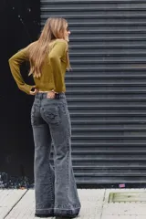 Jean de tiro medio con corte acampanado, confeccionado en denim gris oscuro con efecto lavado. Presenta costuras decorativas y detalles de bordado en la zona de la cintura y bolsillos.