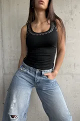 Musculosa negra ajustada al cuerpo, con escote redondo y tiras anchas, decorada con tachas metálicas plateadas alrededor del cuello y los laterales.