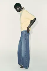 Jersey de punto color amarillo pálido, con cuello redondo y mangas cortas. Presenta un calce oversize y aberturas caladas en los laterales inferiores.