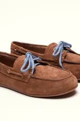 Mocasín tipo boat shoe color marrón, confeccionado en cuero, con cordones de cuero marrón y cordones decorativos azules.