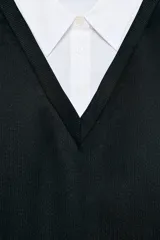 Vestido corto que combina una camisa blanca de manga larga con cuello solapa y botones frontales, con un chaleco de tejido negro de punto con escote en V.